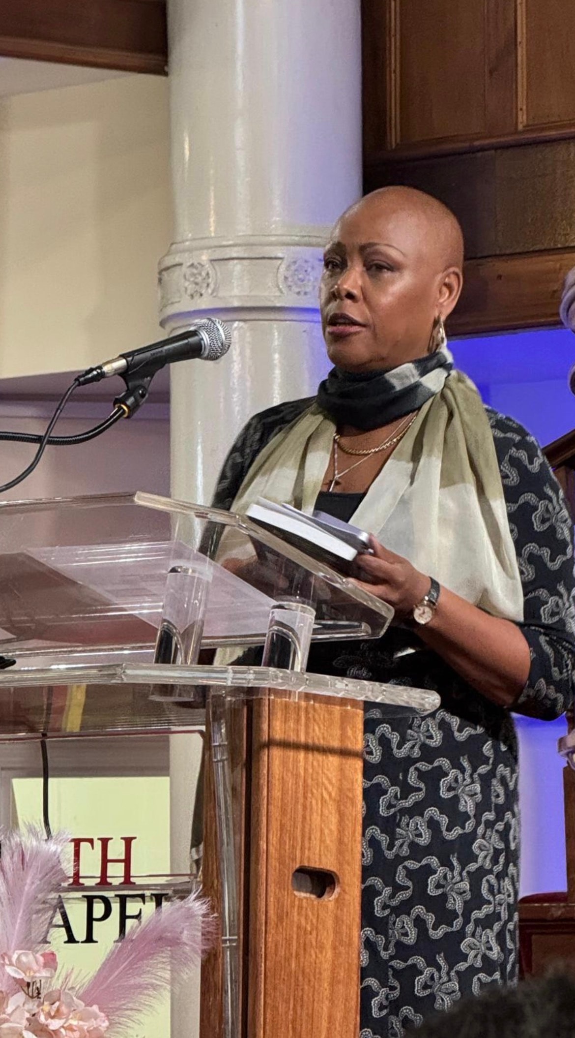 Sharon-Ann Phillips speaking at a chapel podium holding her book Why Me?